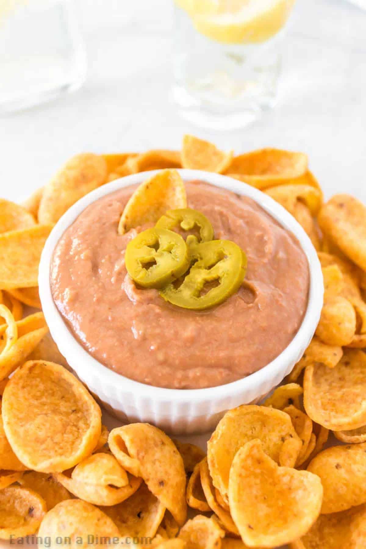 Bean Dip in a white bowl topped with slice jalapenos with a side of Fritos
