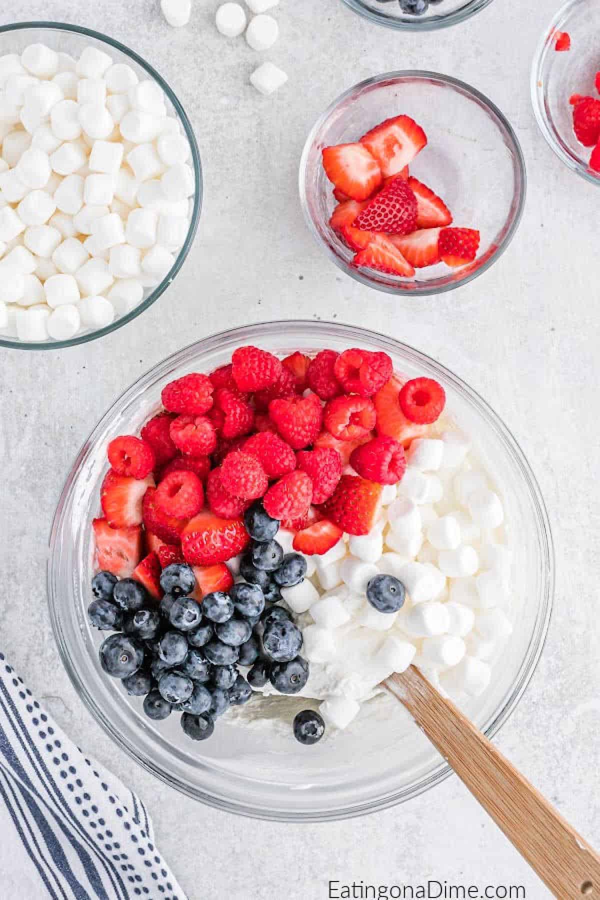 Raspberries, strawberries and blueberries and marshmallows mixed with the cream mixture in a bowl 