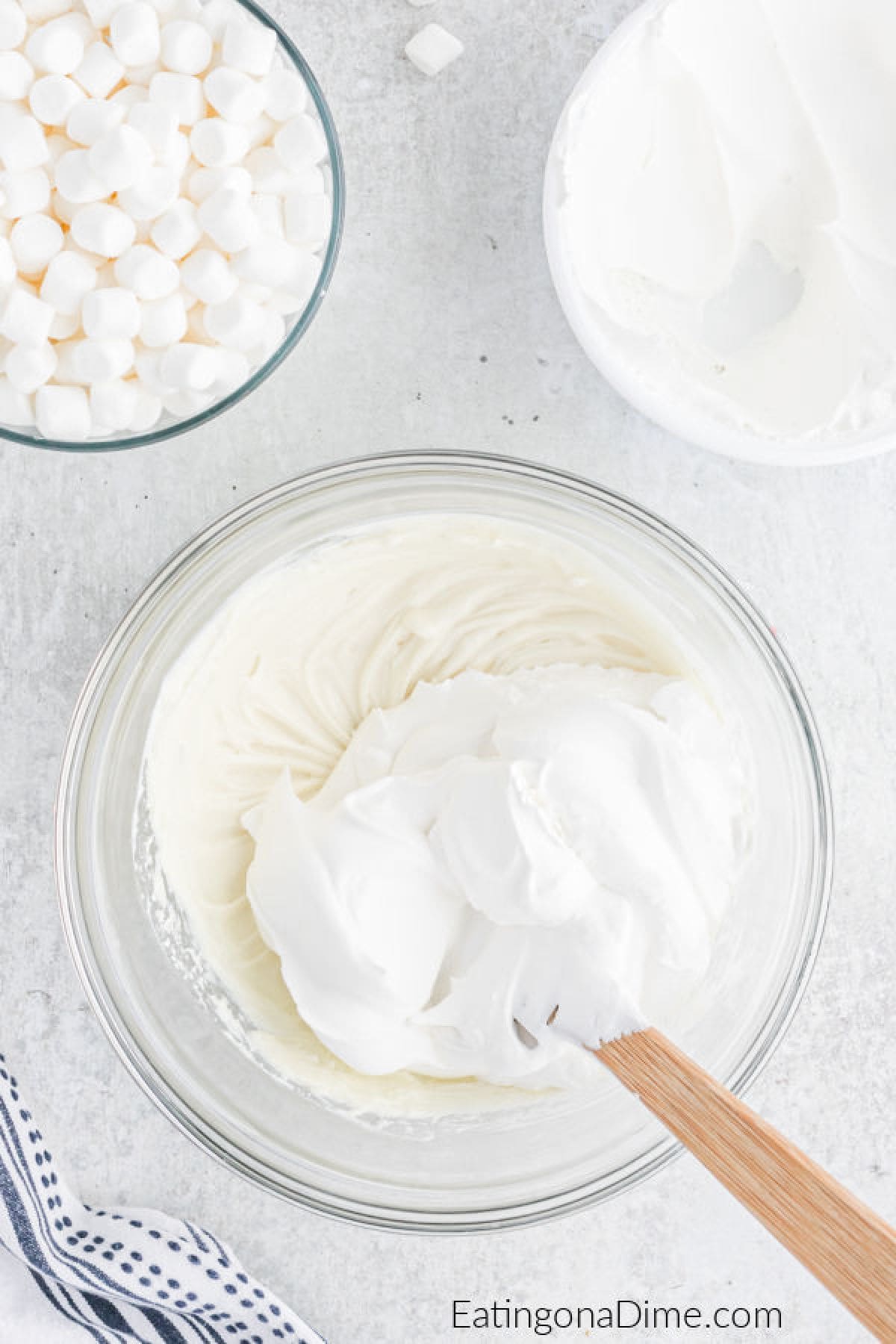 Cream Cheese and whipped cream blended together in a bowl with a small bowl of marshmallows and whipped cream on the side