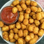 A bowl filled with golden, crispy Air Fryer Tator Tots, with a small round dish of ketchup for dipping placed on the side.