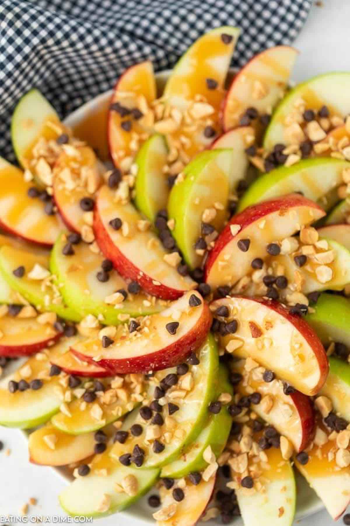 Slice apples on a plate topped with caramel sauce, chocolate chips and chopped nuts