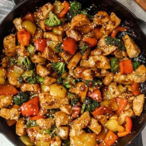 A skillet filled with an easy chicken stir fry recipe—tender chicken pieces, red and yellow bell peppers, broccoli, and glossy sauce—topped with sesame seeds.