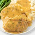 A plate featuring Easy Crock Pot Pork Chops covered in rich brown gravy, served with creamy mashed potatoes and tender green beans on the side.