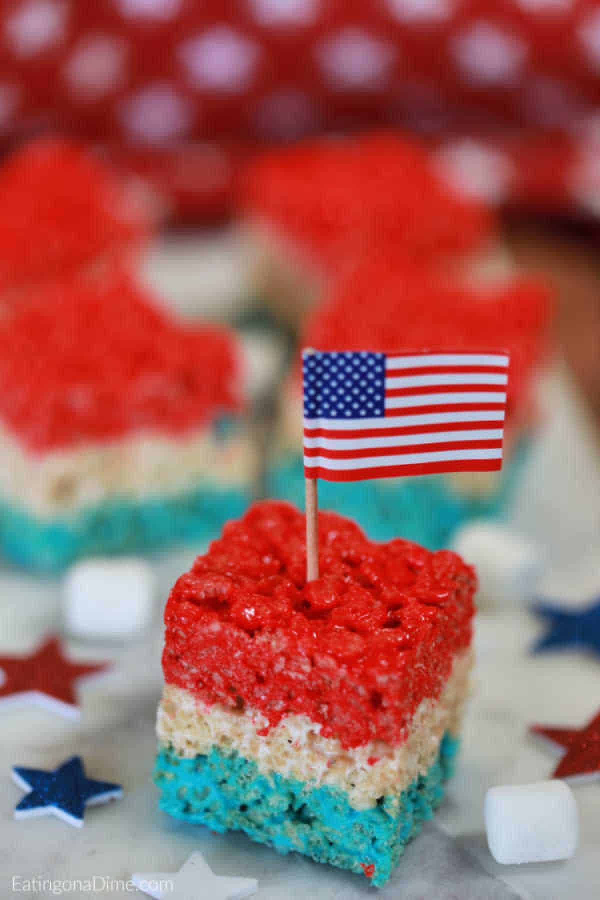 Red White and Blue Rice Krispie Treats cut into square with an American Flag party favor stuck into the treat
