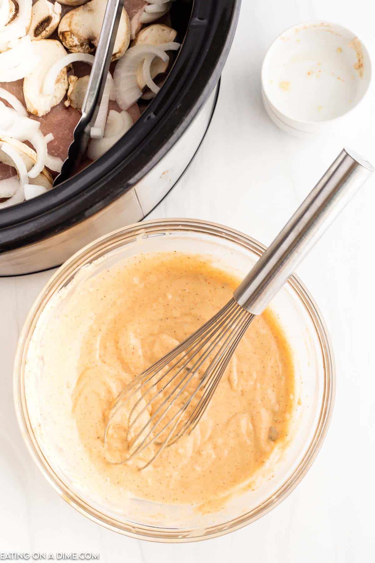 Combining the cream of soups together with broth and seasoning in a bowl with a whisk