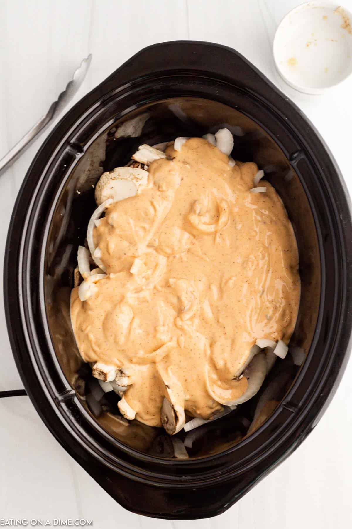 Pouring sauce over the pork chops, onions and mushrooms in the slow cooker
