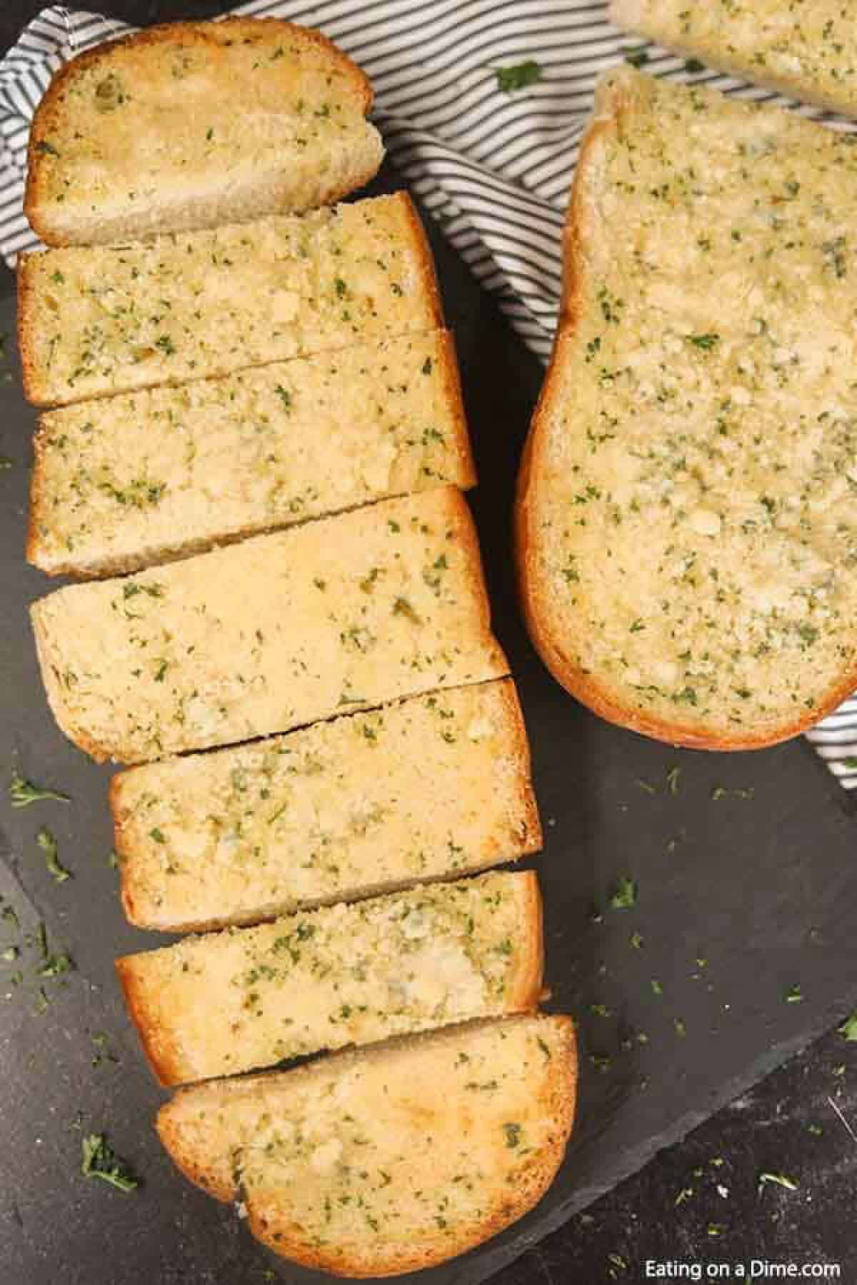 Learn how to make easy homemade cheesy garlic bread. This roasted homemade cheesy garlic bread recipe is the best DIY garlic bread. This home made french bread garlic bread recipe easy is better than Texas toast. Plus learn how to freeze garlic bread. You can make ahead and freeze this simple garlic loaf for later. Make and freezer for a quick and easy Side dish. Can you imagine having homemade garlic bread whenever you want? #eatingonadime #garlicbread #freezebread #freezerrecipes Loafs of Garlic Bread cut into slices