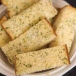 A white plate with garlic bread sticks on it.