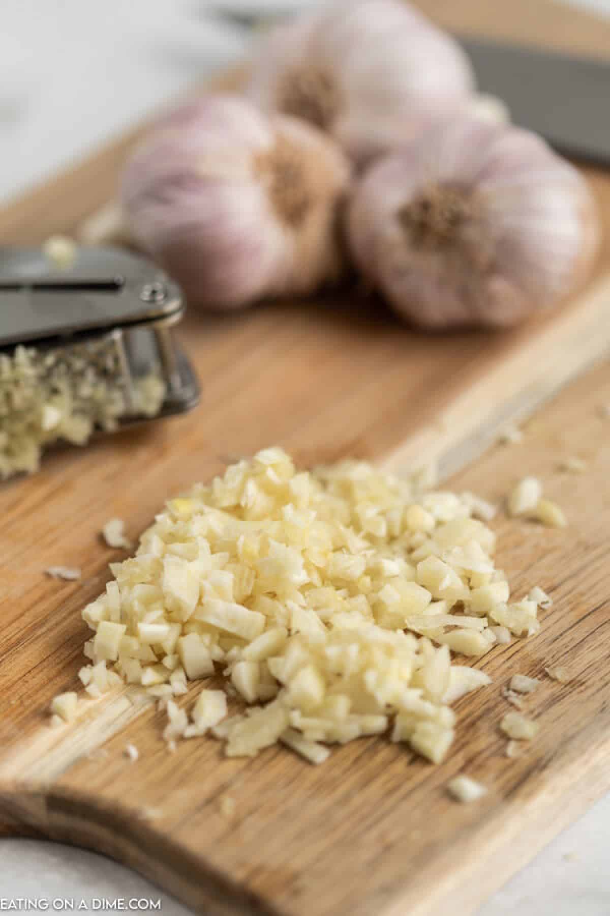 Close up image of minced garlic with a garlic press and garlic cloves.