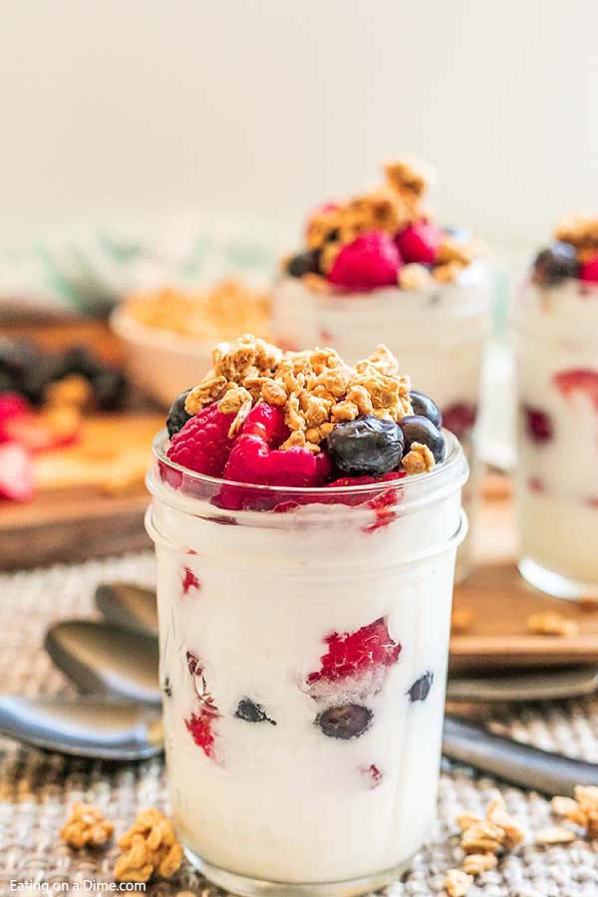 Easy fruit and yogurt parfait has layers of creamy yogurt, granola and fresh fruit. You can make ahead this easy fruit yogurt parfait for a healthy breakfast. This fruit yogurt parfait recipe is so quick and easy. #eatingonadime #easyfruitandyogurtparfait Fruit and Yogurt Parfait in a mason jar topped with granola, raspberries and blueberries