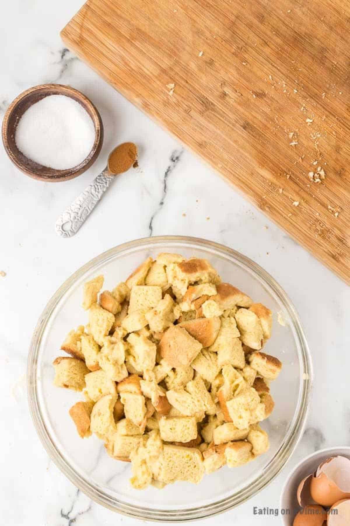 Bread pieces in a bowl mixed with the egg mixture and a small bowl of sugar and teaspoon of cinnamon