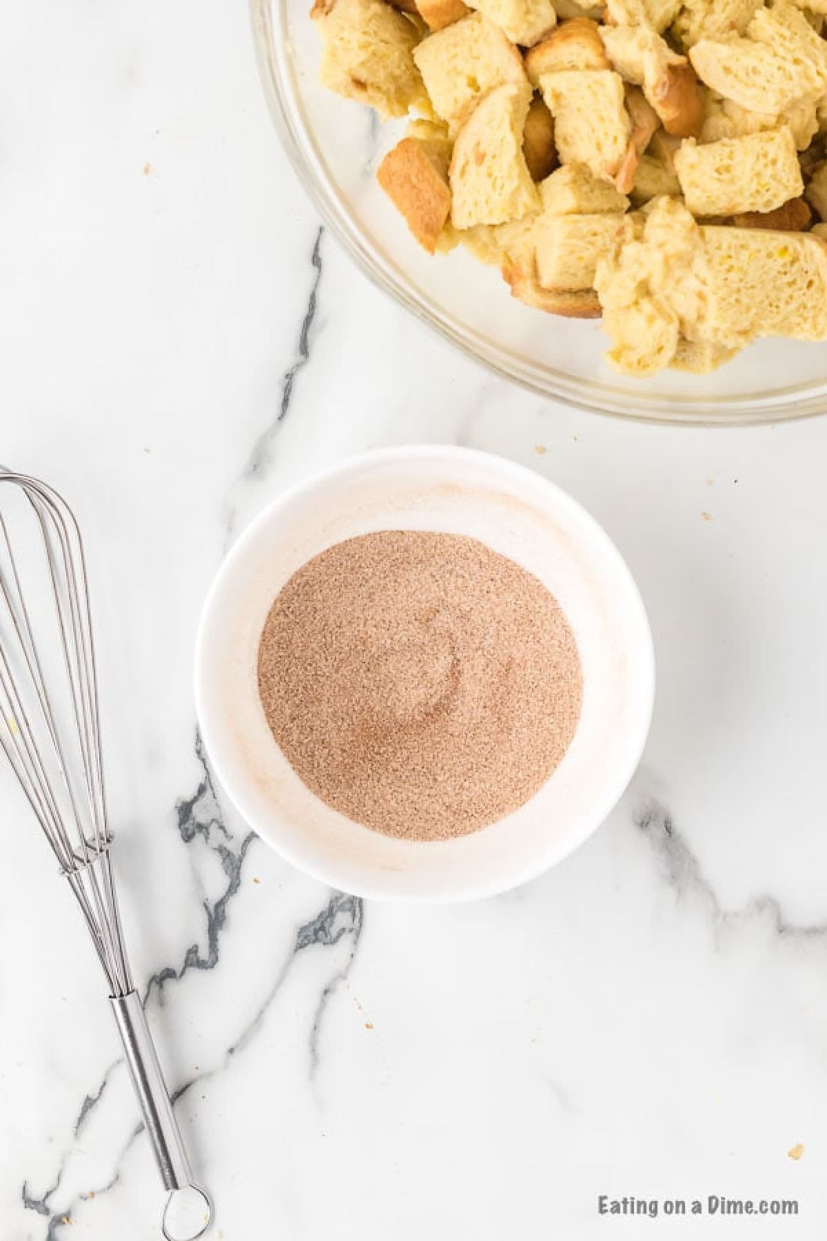 White bowl of cinnamon and sugar mixed together and a bowl of bread pieces in a bowl