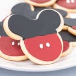 A plate of Mickey Mouse Cookies decorated with red and black icing to resemble Mickey’s head and pants, complete with two white button dots on each treat.