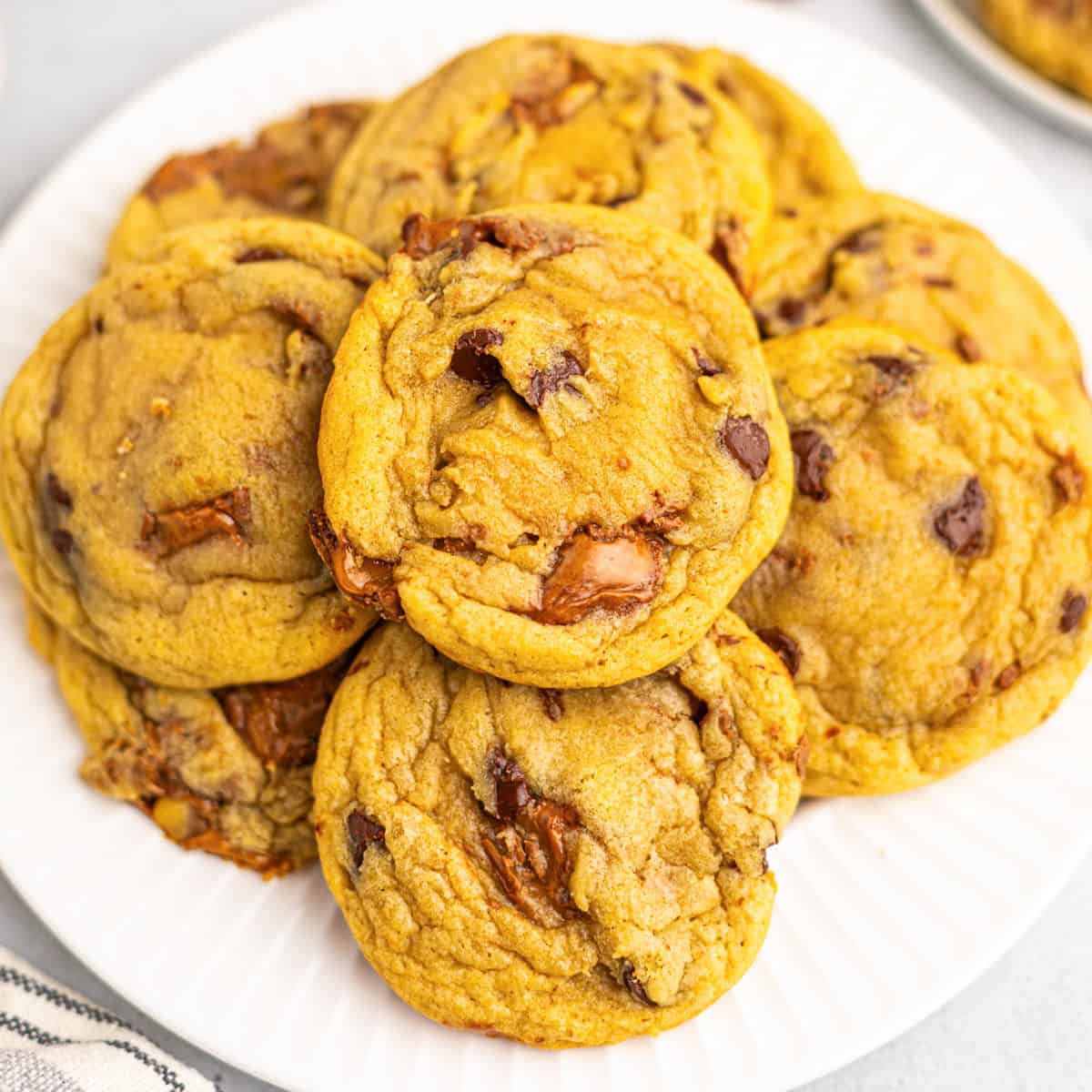 A plate of golden brown Milky Way Cookies piled on top of each other, with visible chunks of melted chocolate throughout.
