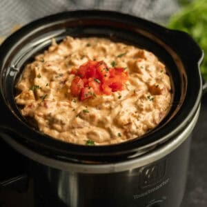 Cheeseburger dip in a small crock pot topped with diced tomatoes.