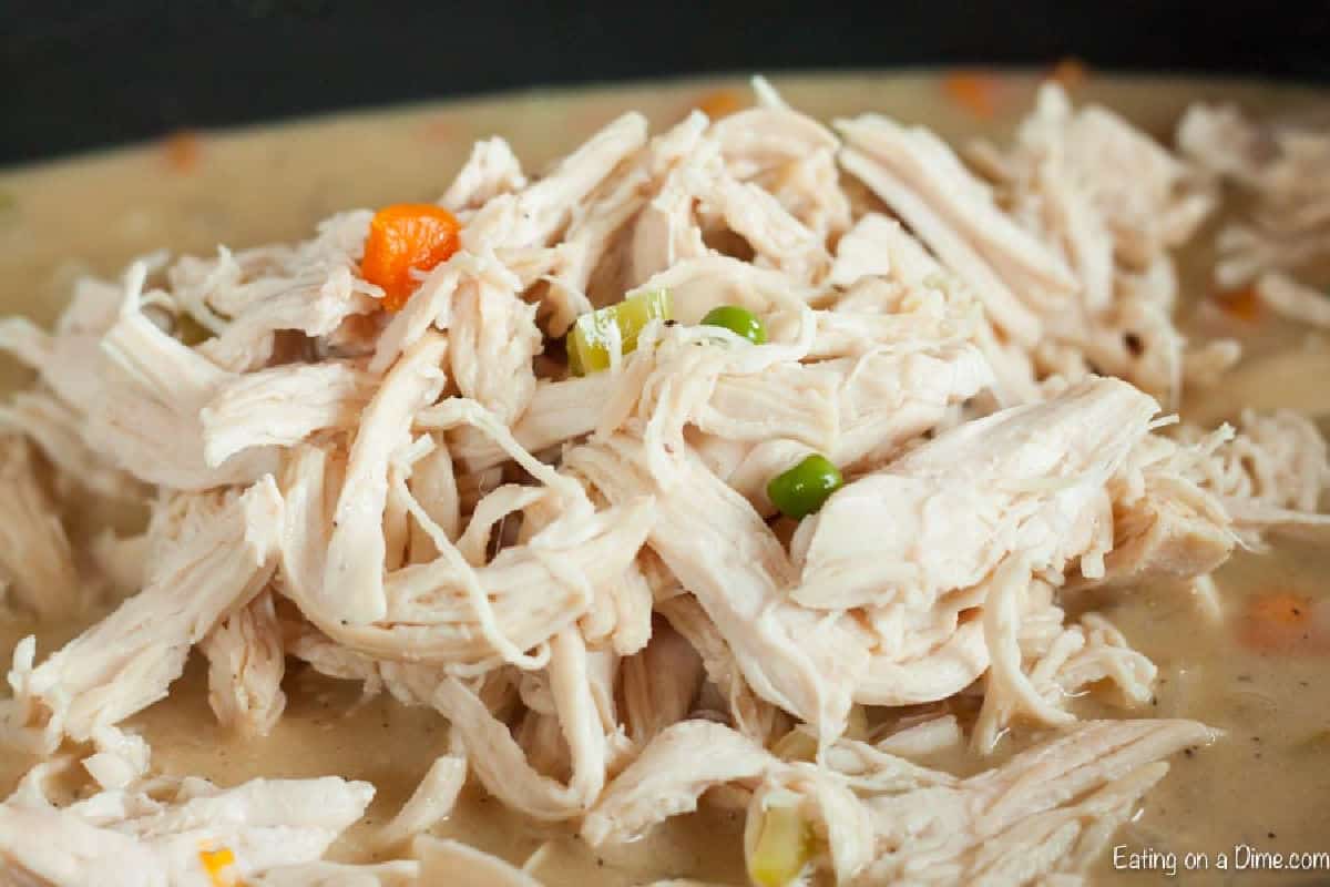 Shredded cooked chicken on top of the soup in the slow cooker
