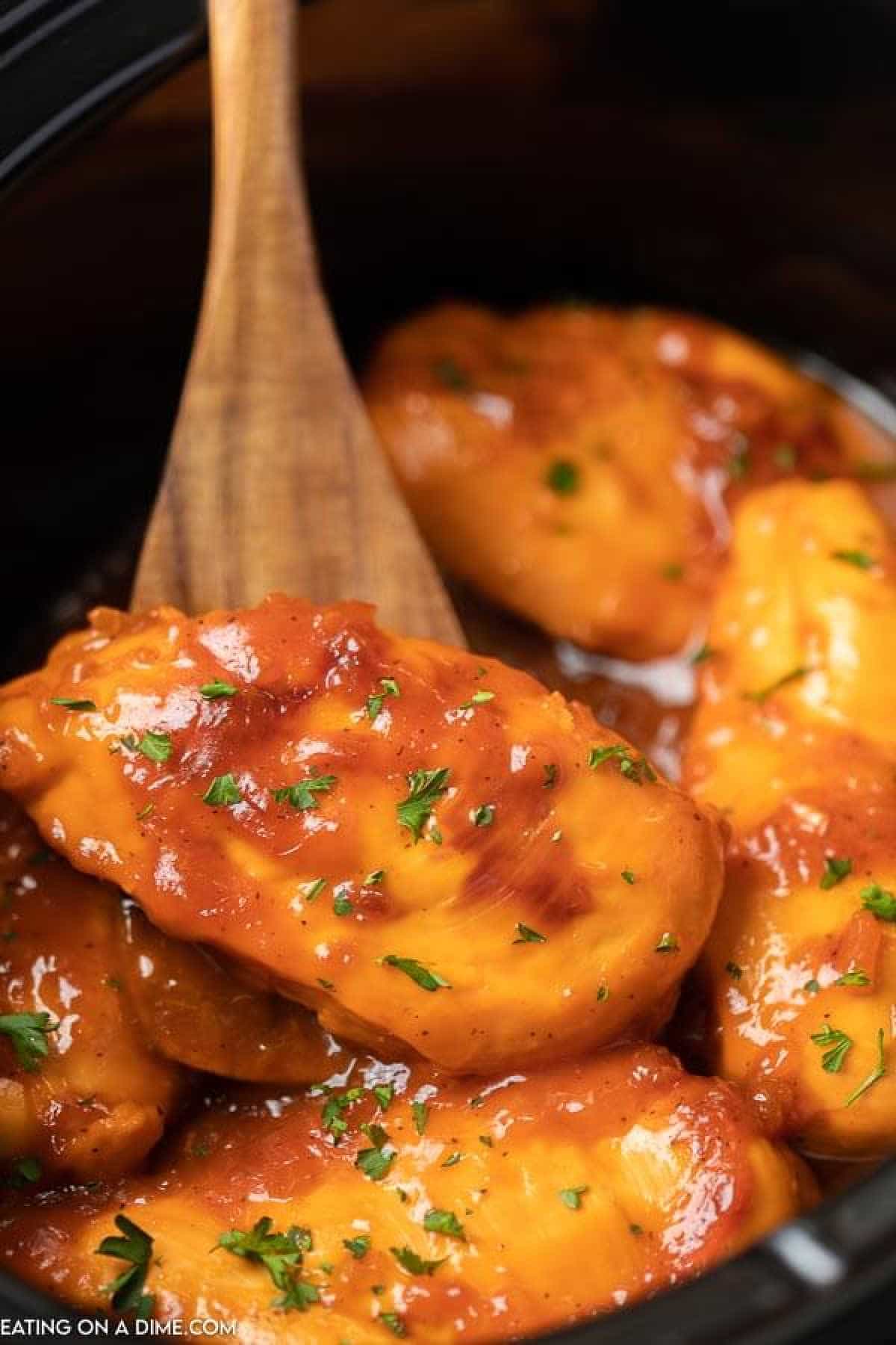 Close up image of catalina chicken in the slow cooker with a serving on a wooden spoon