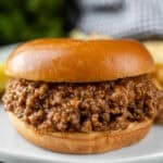 A close-up of a crock pot sloppy joes recipe, featuring a glossy bun and savory ground meat filling, served on a white plate.