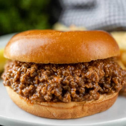 A close-up of a crock pot sloppy joes recipe, featuring a glossy bun and savory ground meat filling, served on a white plate.