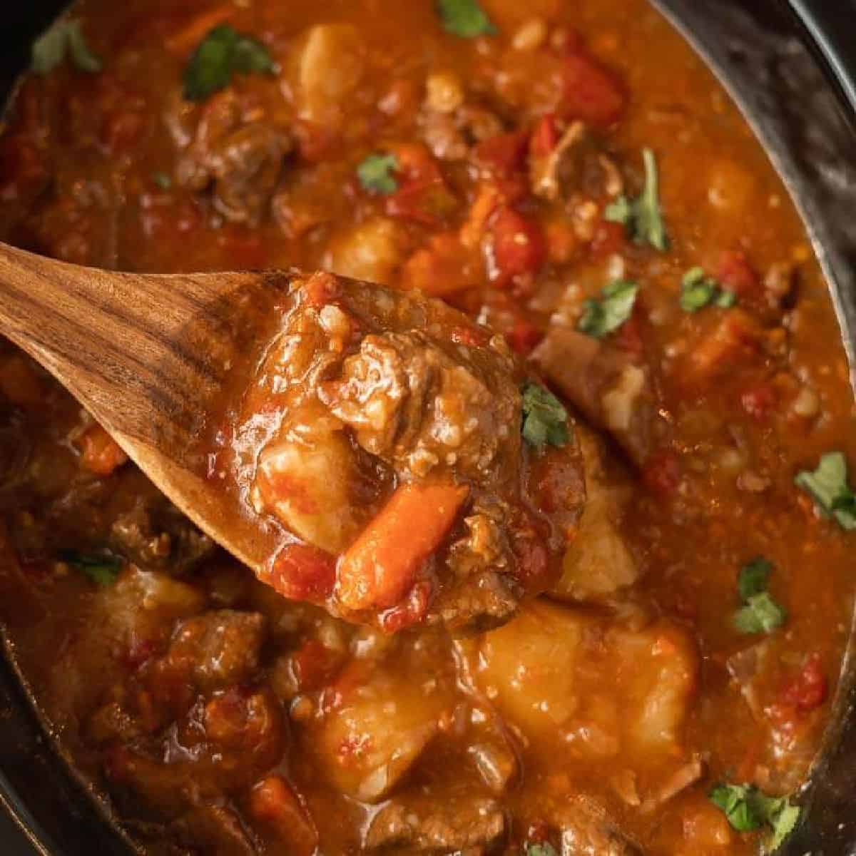 Beef stew in a slow cooker with a serving on a wooden spoon