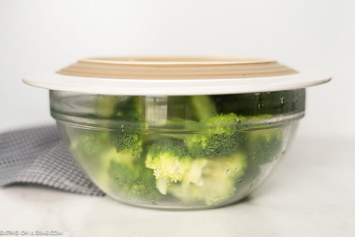 Steamed broccoli in a bowl with a plate on top