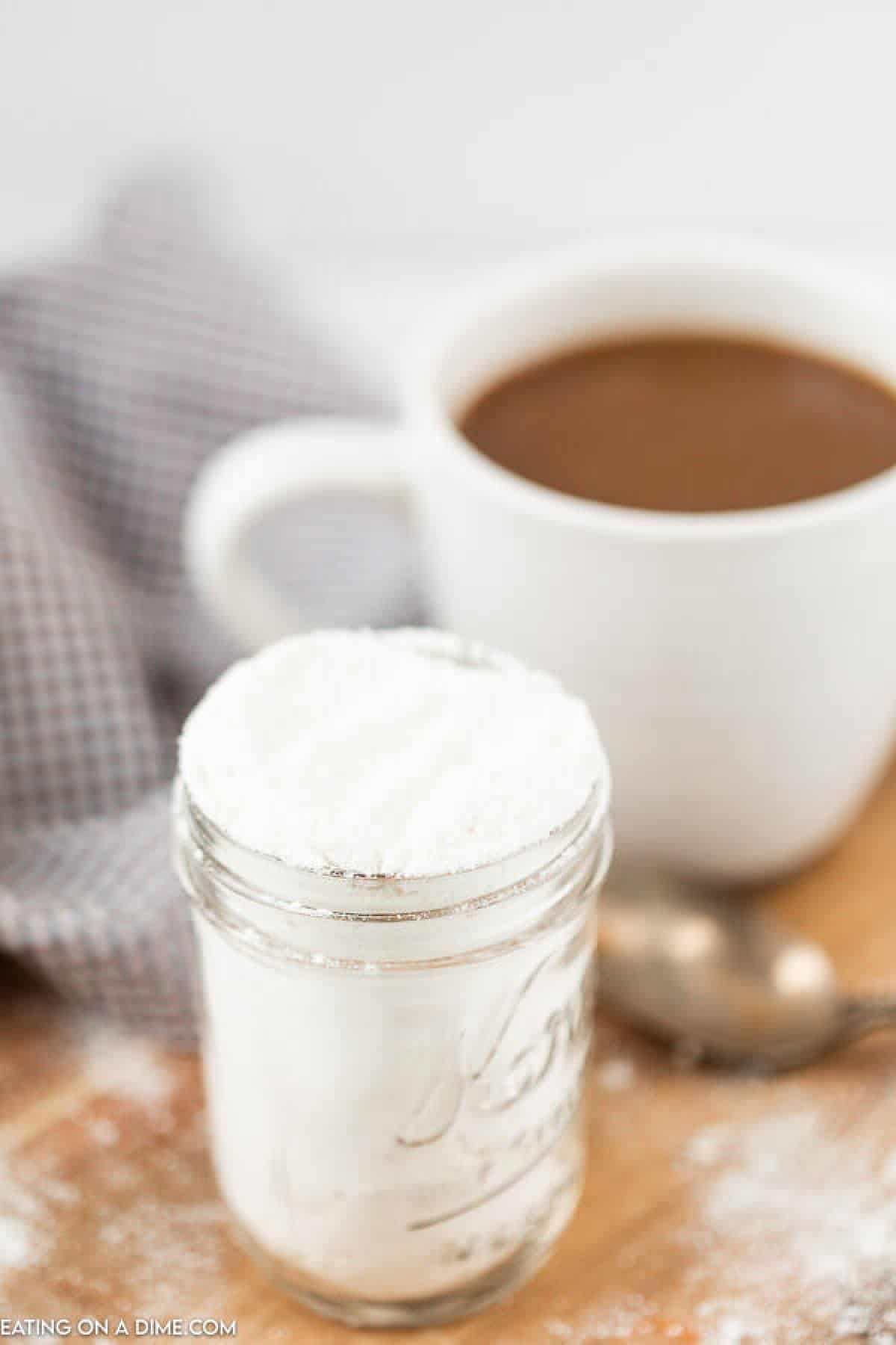 Powdered coffee creamer in a jar with a cup of coffee in the background