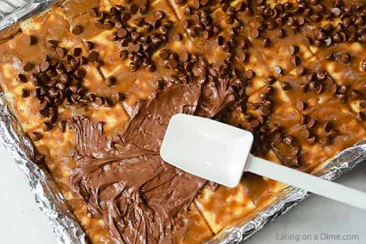 Spreading melted chocolate chips over the crackers coated with the brown sugar mixture on a foil lined baking sheet