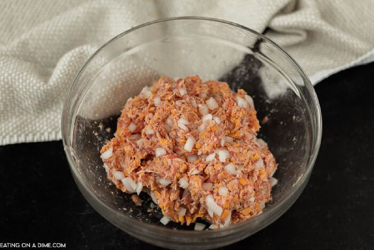 Sausage mixed with chopped onions and shredded cheese in a bowl