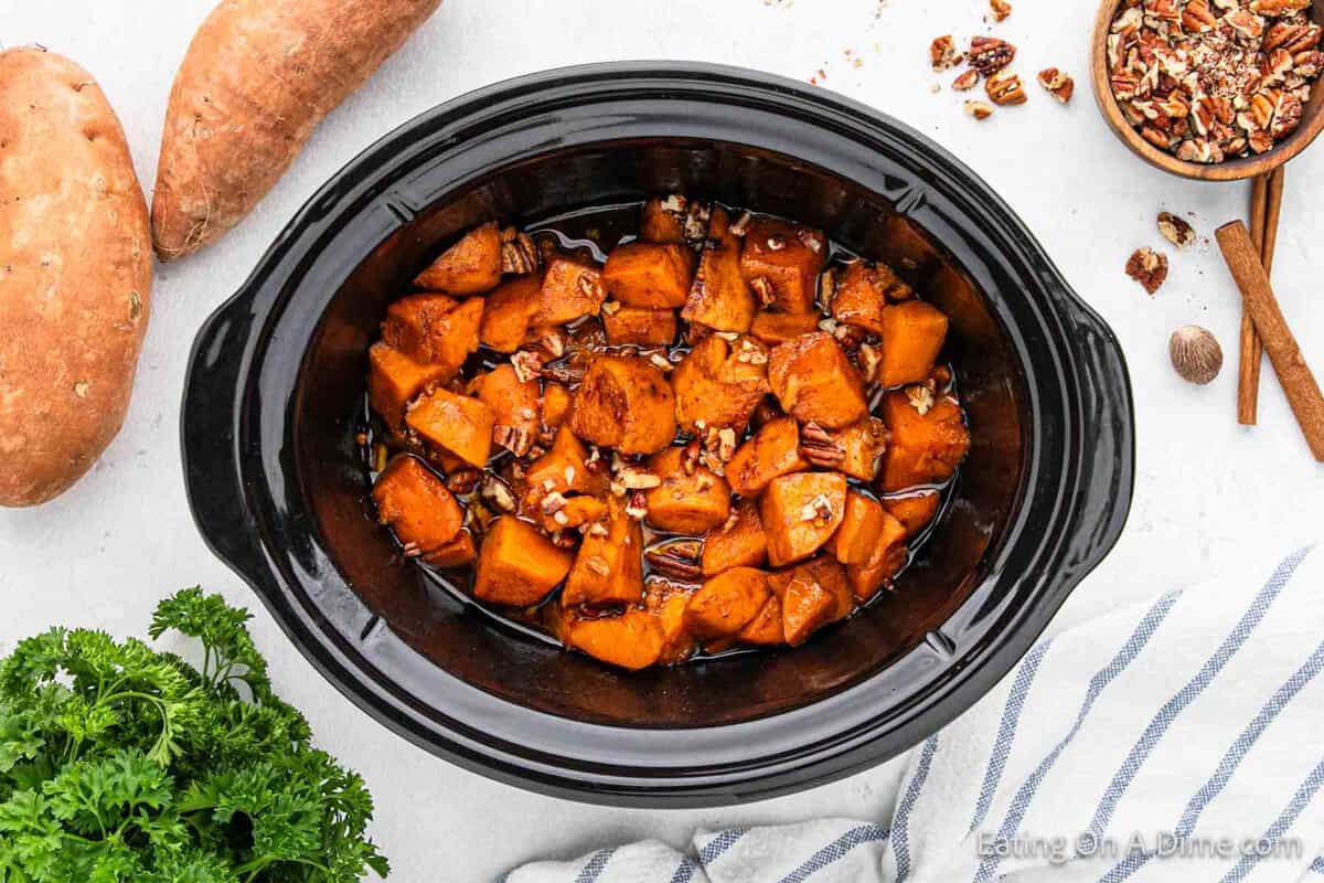 Diced sweet potatoes in a crock pot topped with chopped pecans