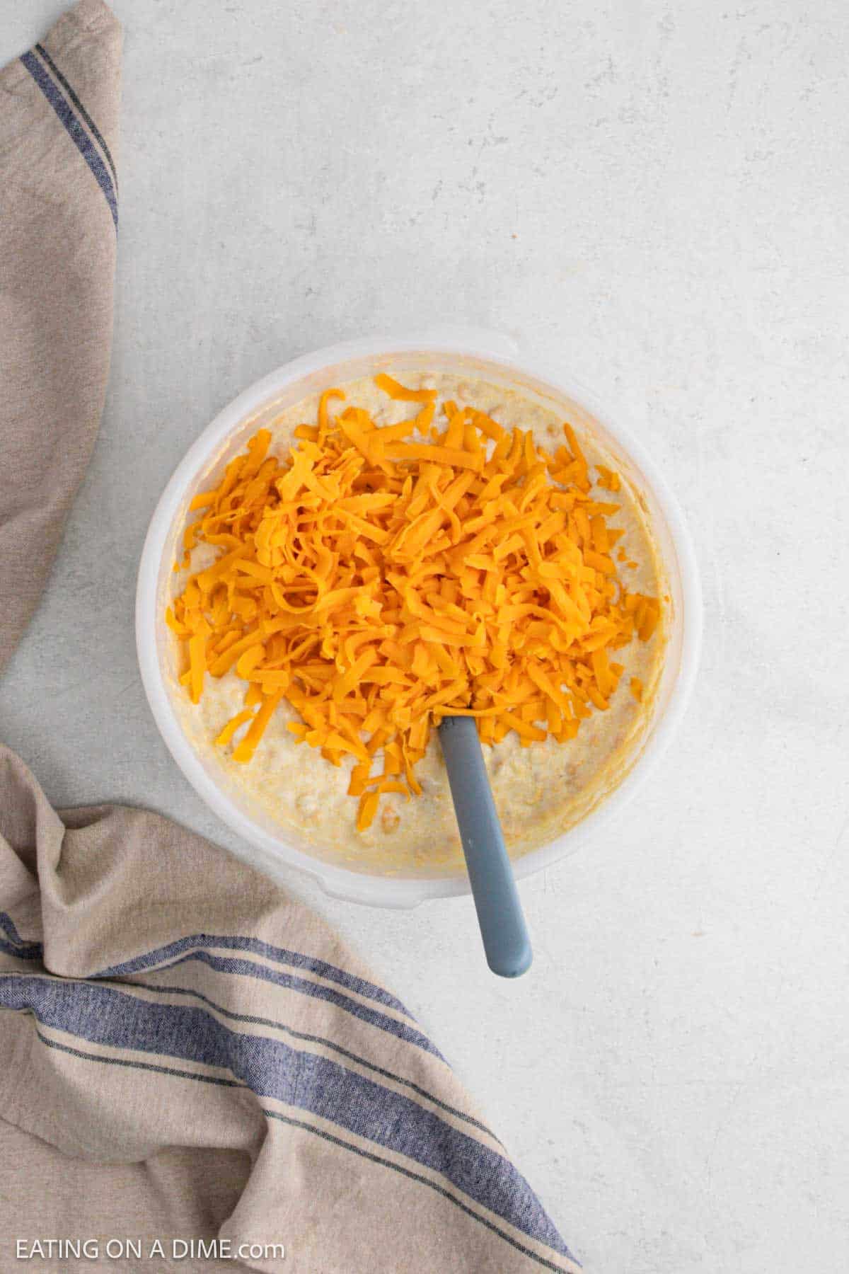 Topping the shredded cheese in the cornbread mixture in a bowl.
