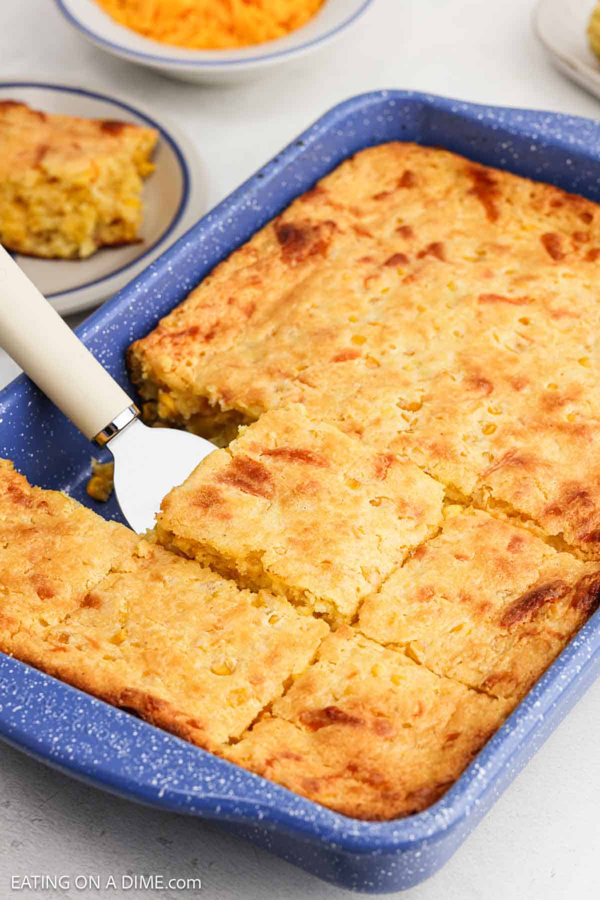 Baked cornbread casserole in a baking dish with a serving on a spatula.