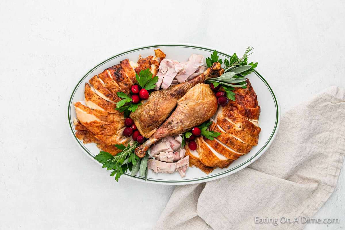 A roasted and sliced turkey is artfully presented on an oval platter, garnished with fresh herbs and cranberries.