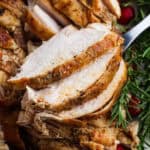 Close-up of juicy, sliced spatchcock turkey breast with crispy, seasoned skin, garnished with fresh rosemary sprigs.