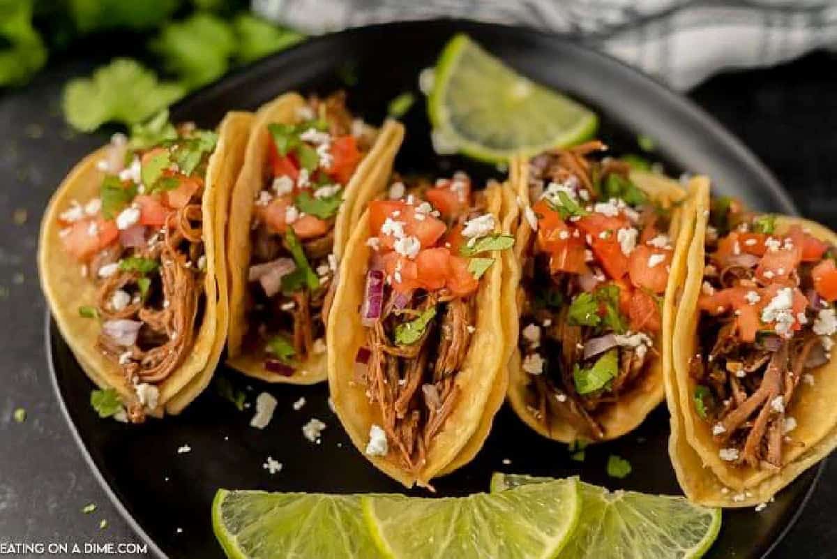 Shredded beef tacos on a plate topped with diced tomatoes and red onions.