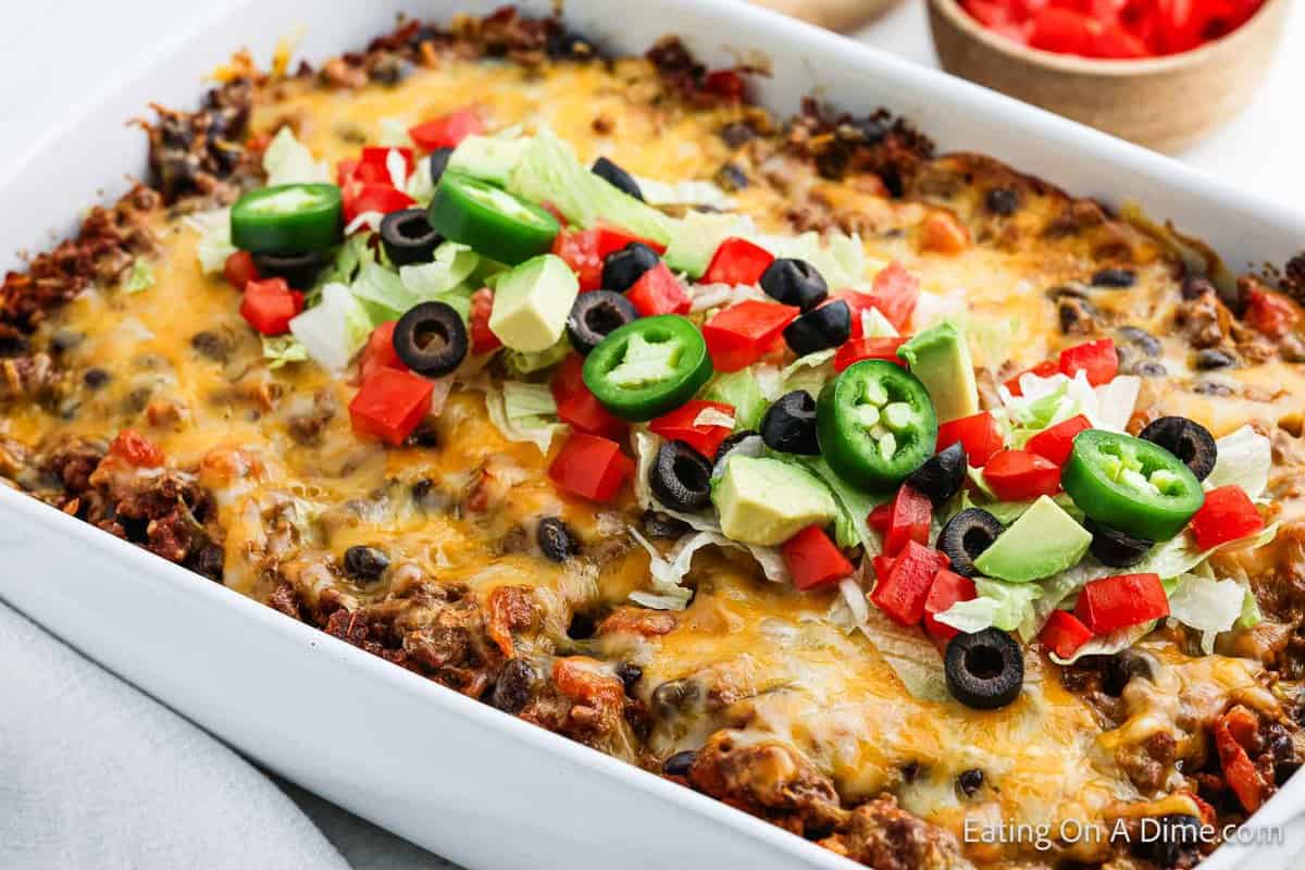 Taco Casserole in a baking dish topped with sliced jalapenos, diced avocados, shredded lettuce and dice tomatoes. 