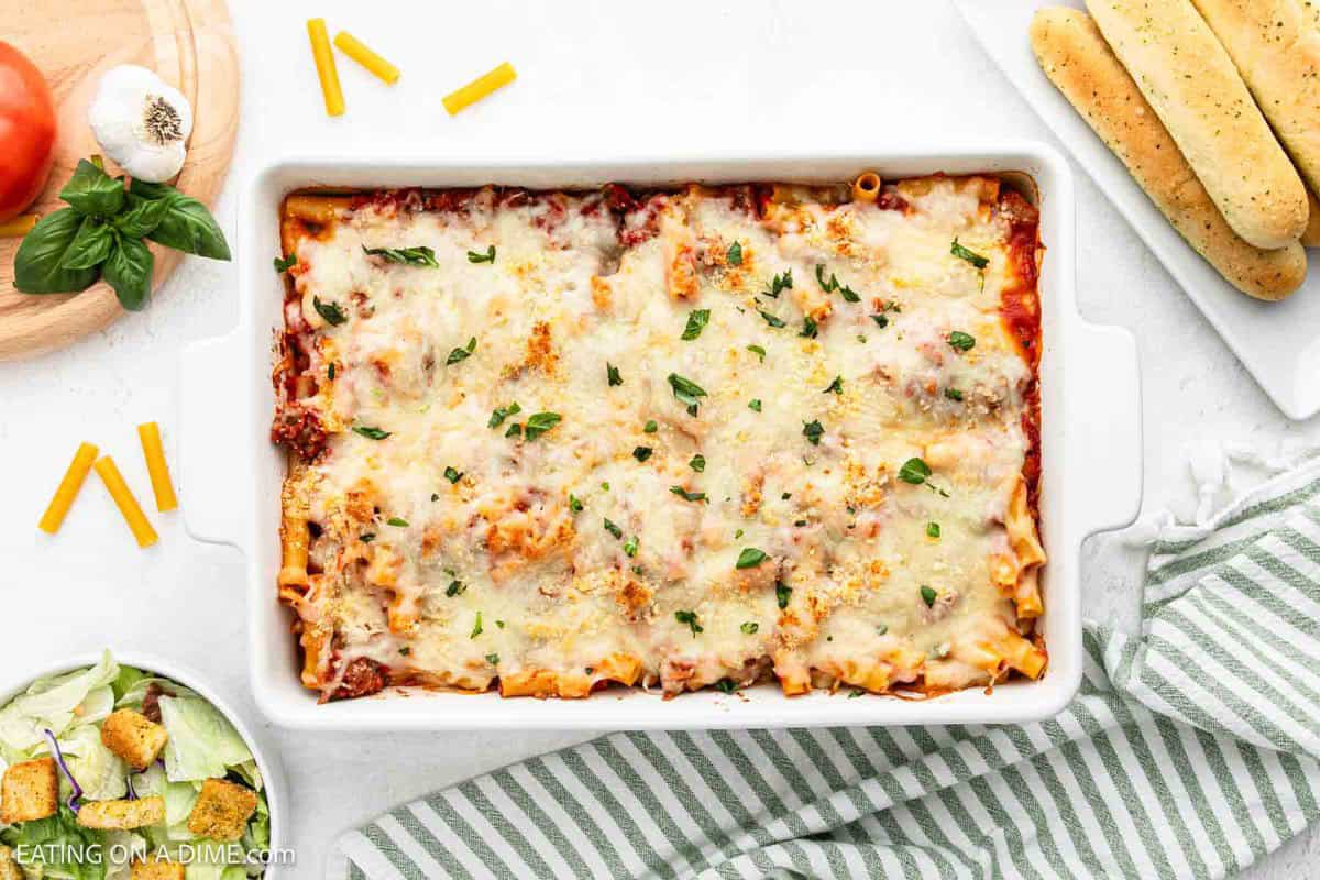 Baked ziti in a baking dish with a side of breadstick and a green salad.