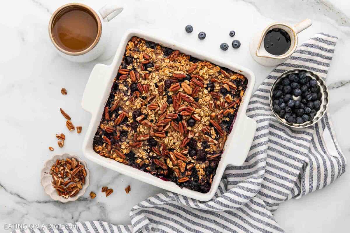 Baked Oatmeal in a square white baking dish with a side of blueberries, syrup and pecans.