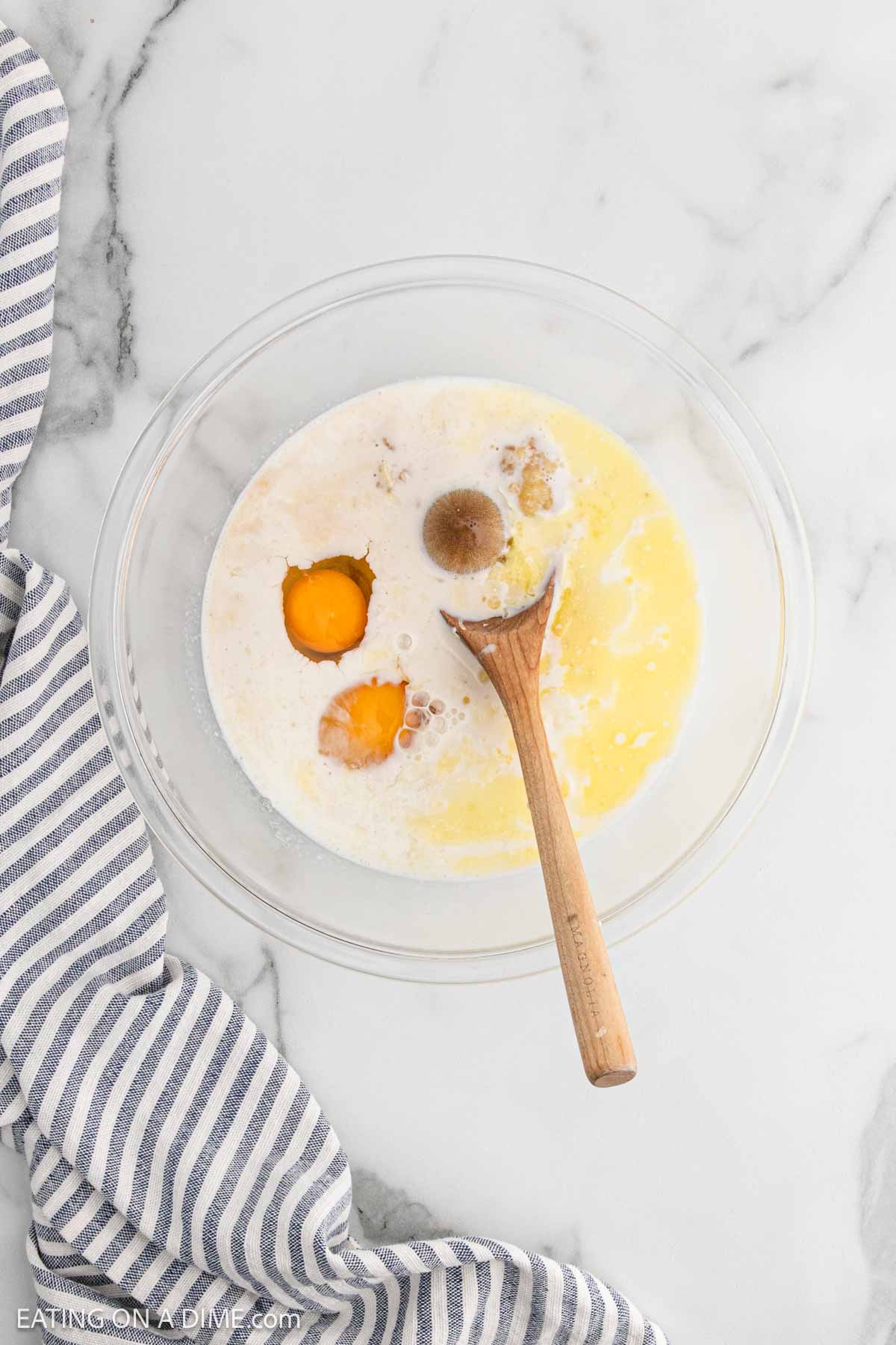 Combining milk, eggs, brown sugar, and vanilla extract in a bowl with a wooden spoon