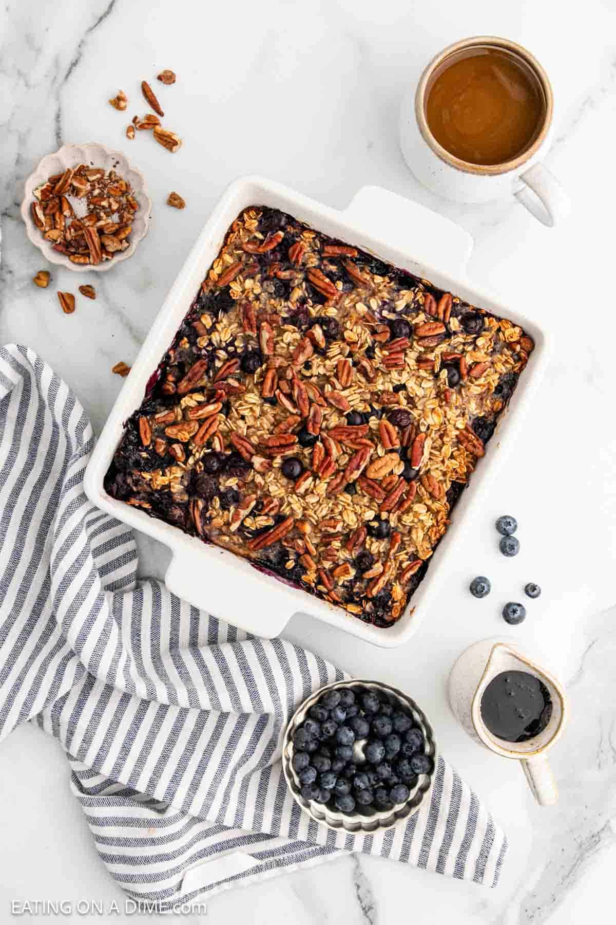 Baked Oatmeal in a square baking dish with a small bowl of chopped pecans, blueberries, and syrup