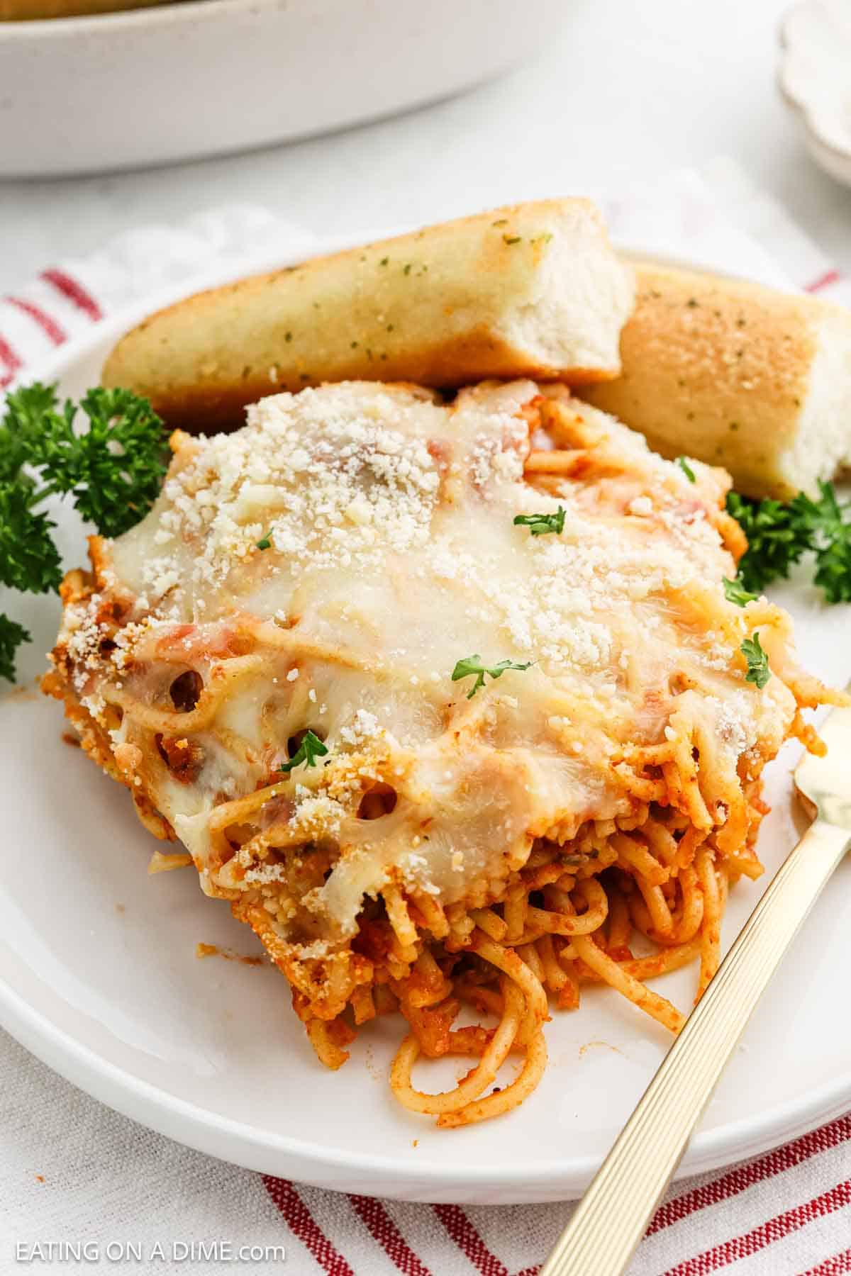 A serving of baked spaghetti on a plate with breadsticks
