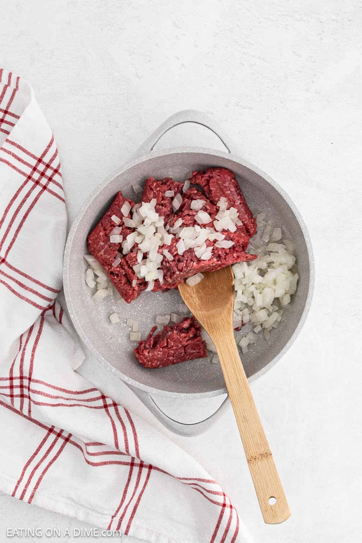 Cooking ground beef in a skillet with chopped onions with a wooden spoon