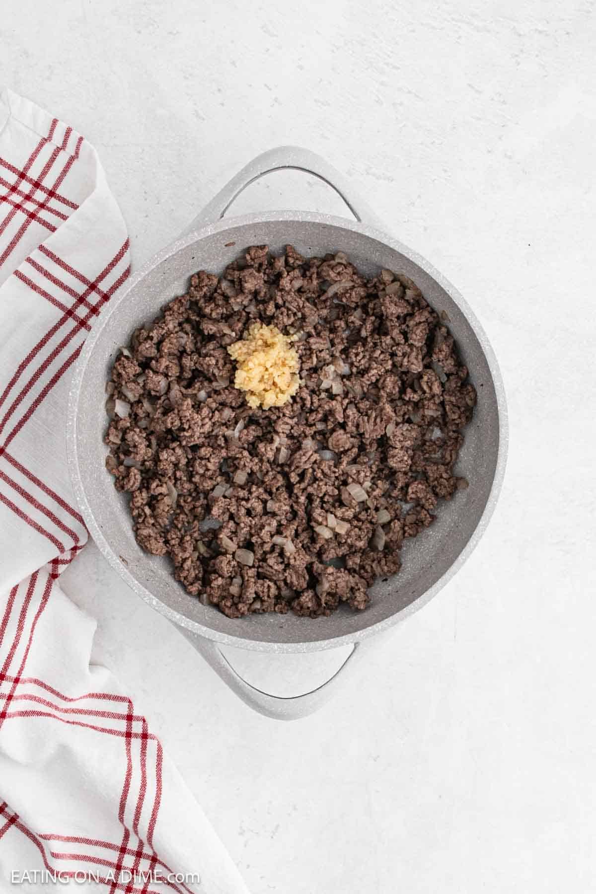 Cooked ground beef topped with minced garlic in a large pot