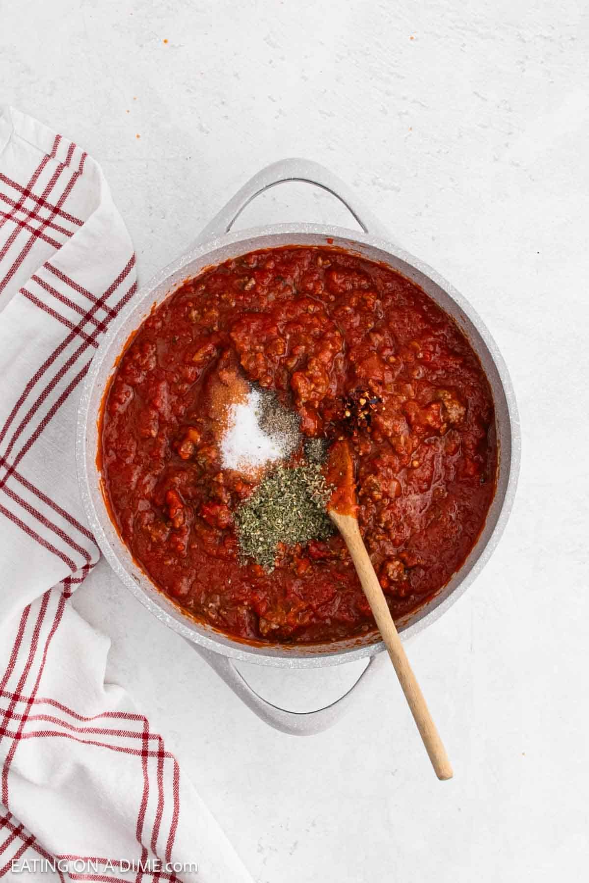 Cooking the tomato sauce and seasoning in the large pot with a wooden spoon