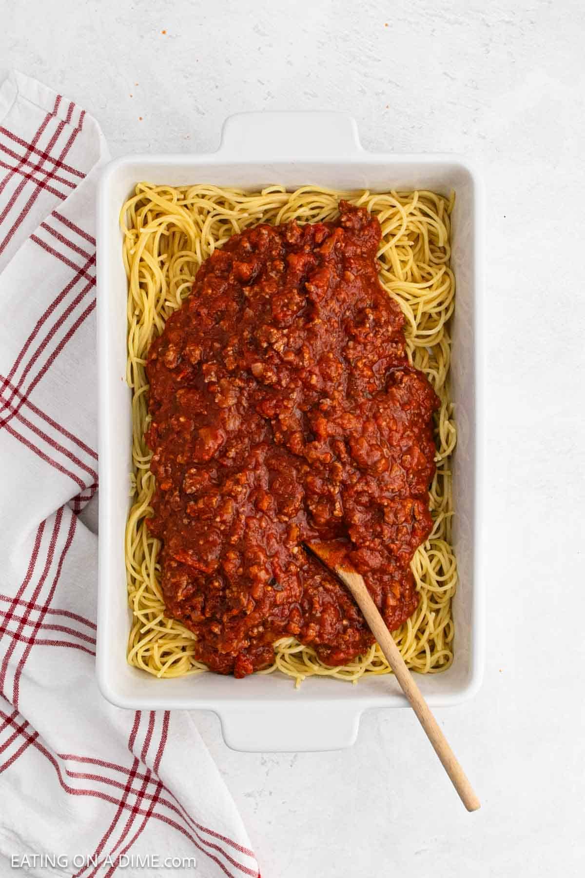 Spaghetti noodles placed in a baking dish topped with tomato meat sauce