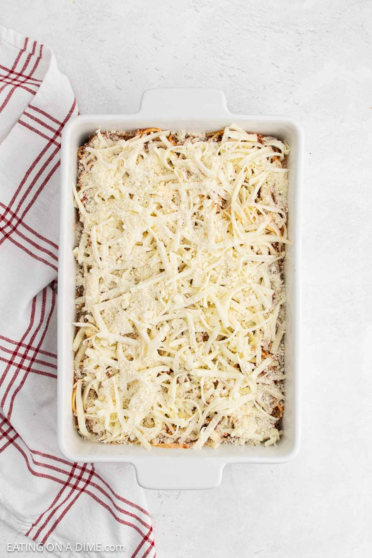 Topping the sauce with shredded cheese in a casserole dish