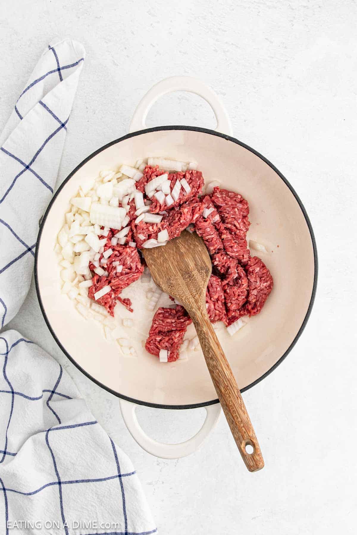 Cooking ground beef and chopped onions in a large pot with a wooden spoon