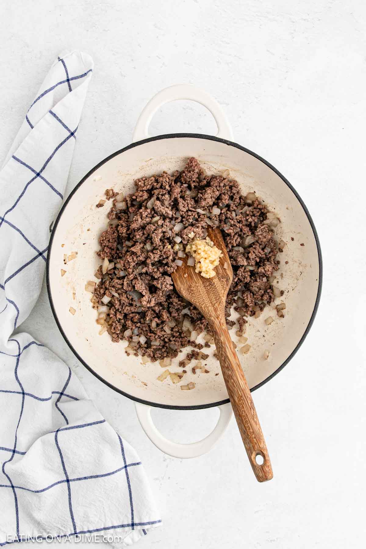 Cooked ground beef in a large pot with minced garlic and a wooden spoon