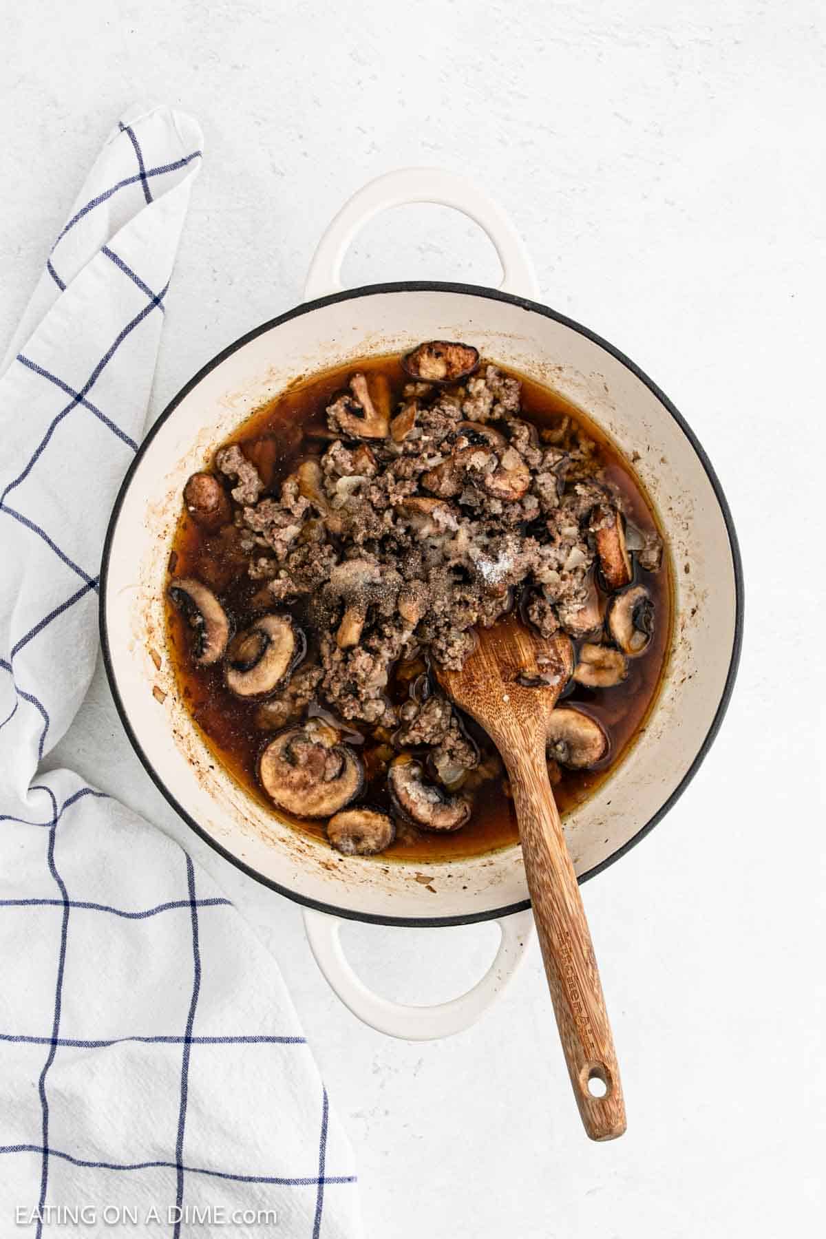 Broth and seasoning poured into large pot with ground beef mixture with a wooden spoon
