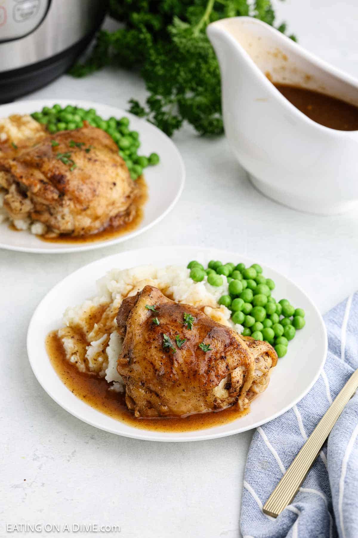 Chicken thighs topped with brown gravy on a plate with a side of mashed potatoes and peas with instant pot and a gravy bowl on the side