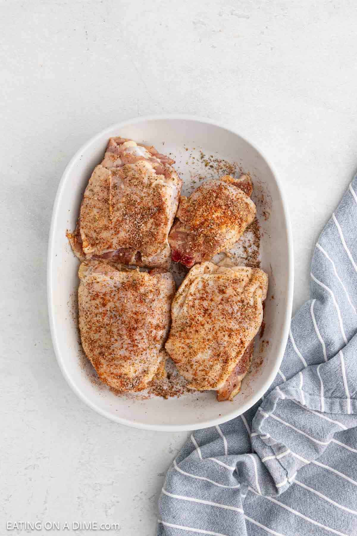 Uncooked chicken thighs in a white baking dish topped with the seasoning blend